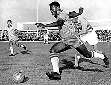 Pelé driblando um defensor durante jogo pelo Brasil, em maio de 1960.