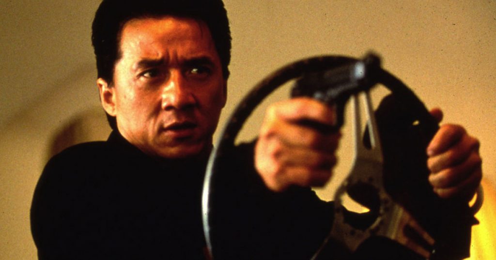Cena de Jack Chan segurando o volante com a arma no filme Hora do Rush de 1998 Imagoi
